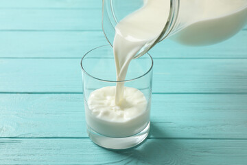 Pouring milk into glass on light blue wooden table