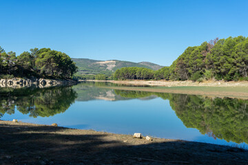Fototapeta na wymiar Reservoir landscape with nice reflections of the forest in the water on a day with blue sky