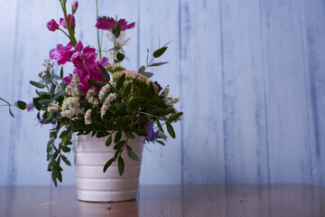  Multicolored wildflowers stand in a white vase against a blue wall 