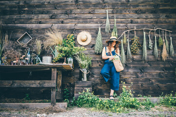 Attractive girl wearing straw hat and blue denim dungarees relaxing near bouquets of aromatic...