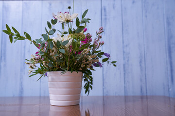  Multicolored wildflowers stand in a white vase against a blue wall 