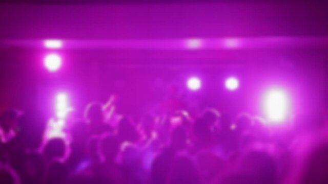 Blurred video of people dancing in a club against the backdrop of a DJ stage with pink lights. Dynamic club background for the video template.