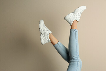 Woman wearing sneakers on beige background, closeup