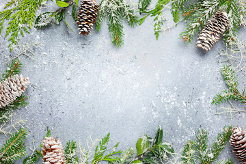 Christmas or winter background with a border of green and frosted evergreen branches and pine cones...