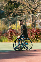 Young handsome man in wheelchair at basketball playing ground