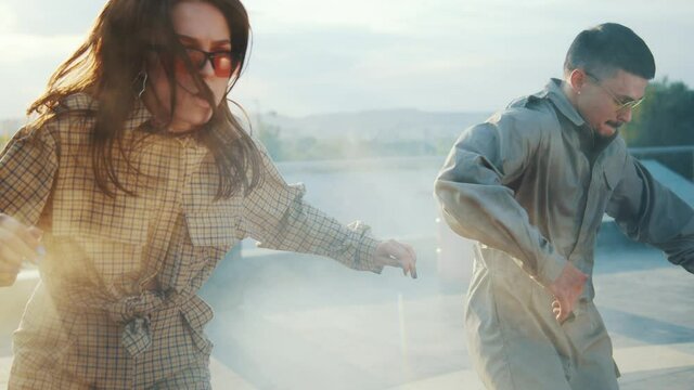 Skillful contemporary dance artists dancing in smoke and sunset lights on rooftop. Competitive male and female talented people performing street hip hop break dance together.
