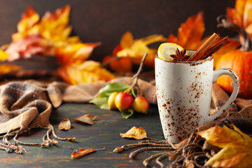 Autumn or winter spice tea in mug with seasonal fruits, berries, pumpkin and leaves on wooden table.