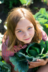 Beautiful girl sitting in a cabbage field. Girl with ears of cabbage leaves for the camera. The girl smiling, cheering and having fun.