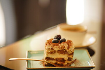 Cake decorated with fresh berries in a plate on the table in a cafe. Tiramisu cakes and coffee on table