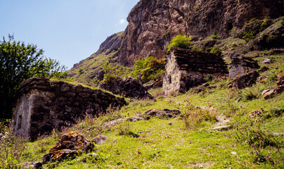 Fototapeta premium Ancient stone houses in green mountains. Amazing landscape with aged stone buildings located on green grassy slope of rocky mountain in sunny summer day