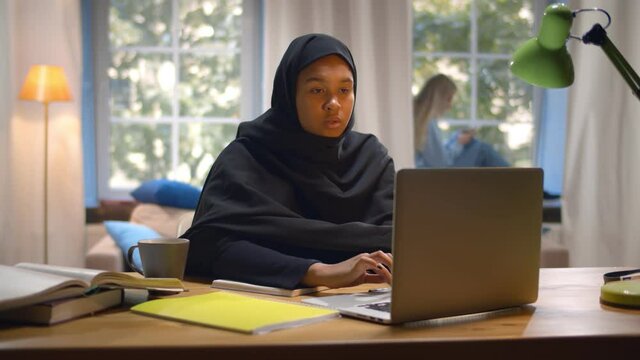Islamic young woman student wearing abaya and typing on laptop in college common room
