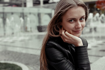 Fototapeta premium Portrait of confident young woman. Femal model sitting on a bench and looking at the camera.The girl wearing black leather jacket 