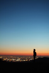 Fototapeta premium Silhouette of a person up on a hill with city lights in the background 
