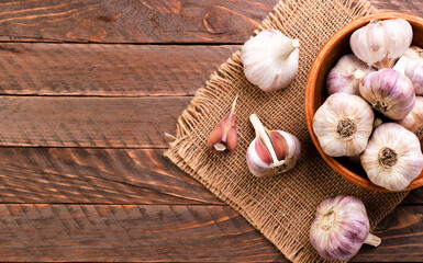 Garlic in a plate whole and a clove of garlic on a wooden background, top view. Copy space