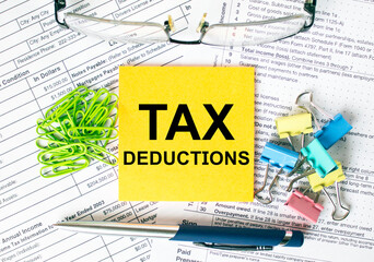 Orange sticker with text Tax Deductions. Colored stationery clips, green paper clips and eyeglasses