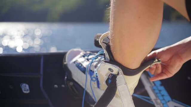 Putting on a wakeboard before a riding session on a lake on a sunny day, strapping board boots