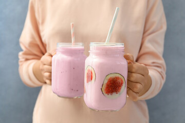 Woman holding fig smoothie on light blue background, closeup