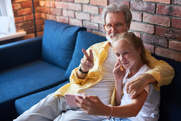 kind senior man take selfie with granddaughter, bearded male enjoy time with grandchild at home,...