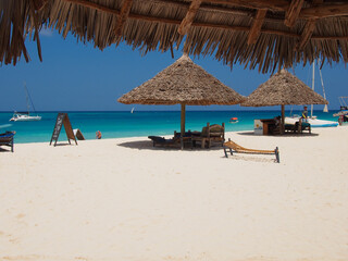 Zanzibar island, Tanzania - 08/15/2020: Sunny beach day, white sand, blue Indian ocean and  sun umbrellas. Copy space for text.
