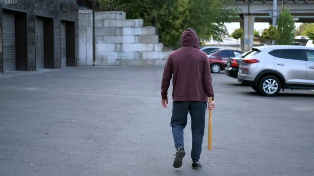 robber vandal with a bat goes along the cars and is plotting something