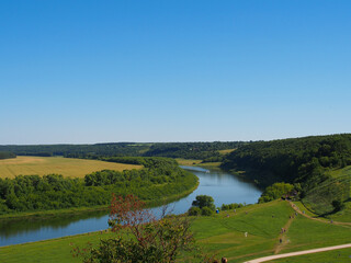 Obraz premium Green grass, river, field and blue sky. Copy space for text.
