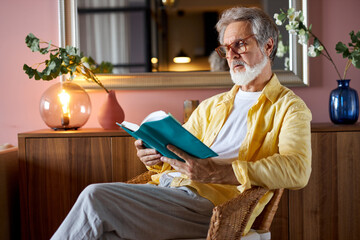 elderly bearded mature man read book at home, enjoy free time alone, sit on chair