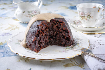 Traditional Australien plum pudding with vanilla rum sauce offered as close-up on a design plate