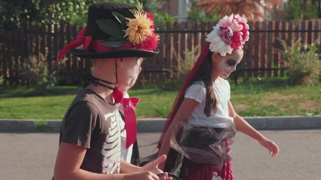 Handheld tracking shot of boys and girl in halloween costumes walking down street together while trick-or-treating in neighborhood