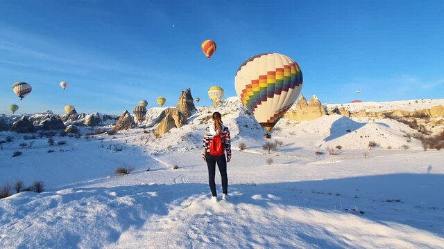 Woman walking in the mountains in winter time. Hot air balloons on the background.