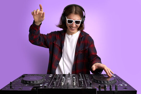 positive male DJ playing music on purple background, caucasian long haired man in casual wear perform club music, wearing headphones