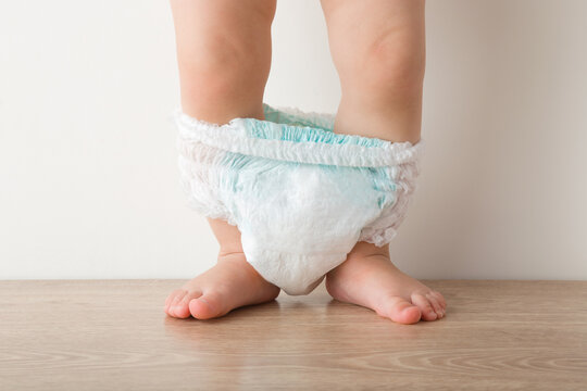 Baby legs with white diaper pants standing on wooden floor. Closeup. Front view.