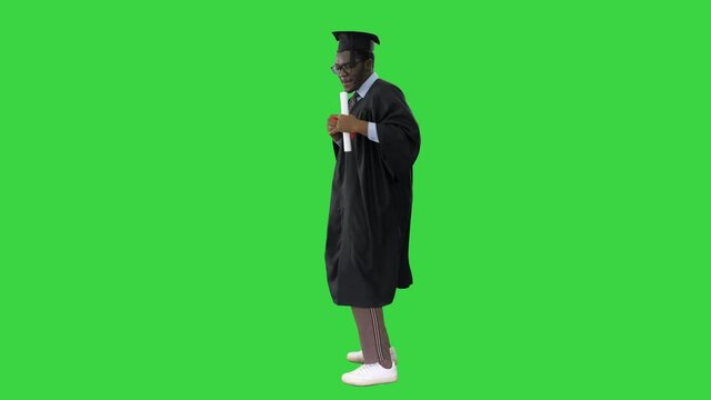 Excited african american male student in graduation robe dancing happily with his diploma on a Green Screen, Chroma Key.