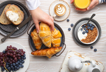 Beautiful morning breakfast gathering with fresh croissants, granola with yoghurt and berries,...
