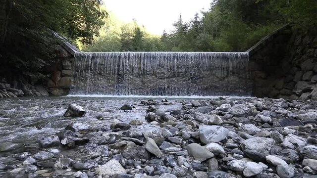 renewable energy, barrage of a wild river, flowing water with a bed of gravel stones, framed  by green trees