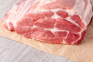 A piece of uncooked meat of pork neck on paper on gray table. Close up view.