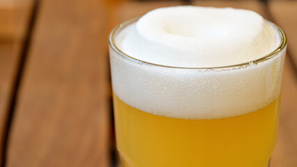 Close-up of a glass with wheat unfiltered beer and lush white beer foam on a wooden table. Traditional light alcoholic drinks. Space for text. 