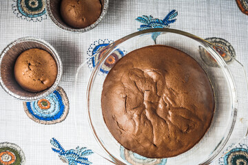 homemade chocolate cake and cupcakes on the table. round baked chocolate cake in glass baking bowl. Brown muffins in foiled baking forms. Tasty morning breakfast