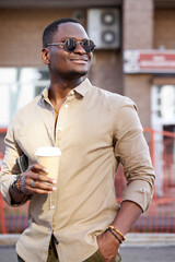 portrait of fashionable cool black man walking outdoors with cup of coffee, stylish african guy in sunglasses enjoy, in city streets