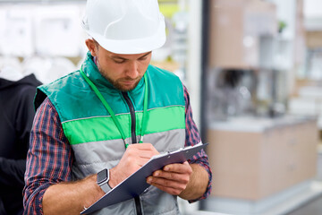 caucasian man is checking supplies on document with an engrossed expression in warehouse, in uniform