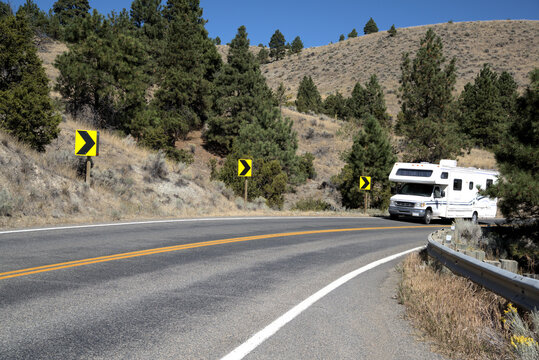 Motor home ascends a Montana mountain slope with warning signs marking the curve.