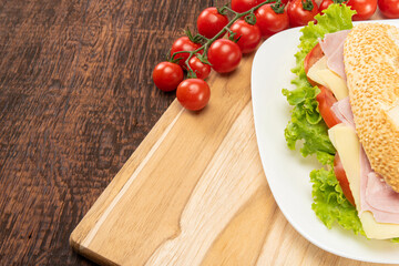 Sandwich of mayonnaise, cheese, ham, tomato and lettuce placed on a white plate on a rustic wooden table with cherry tomato, selective focus.