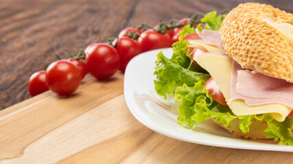 Sandwich of mayonnaise, cheese, ham, tomato and lettuce placed on a white plate on a rustic wooden table with cherry tomato, selective focus.