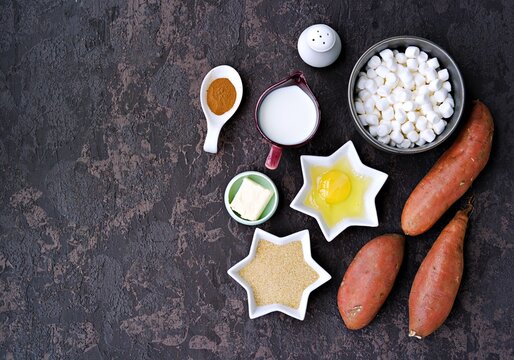 Ingredients for cooking sweet potato casseroles with marshmallows, a traditional Thanksgiving dessert on brown concrete background. American cuisine. Sweet potato recipes.
