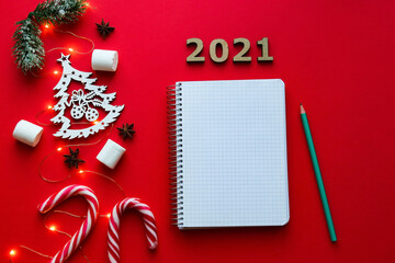 Christmas decorations and notebook for writing goals or results of the year on bright red background. New Year goal list 2021. Top view, flat lay. Festive and holiday concept