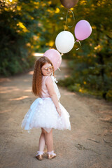 Little redhead holds balloons out in the nature. Celebration concept