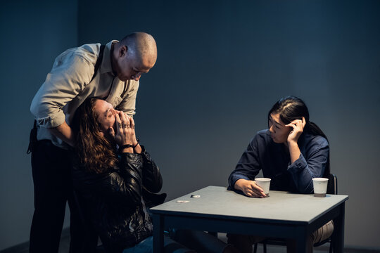 A suspect in a police station laughs madly during an interrogation conducted by investigators.