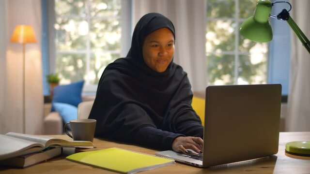 Portrait of happy arabic woman with hijab smiling and using laptop computer indoors