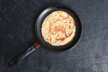 Tasty pancake in a black pan on black background