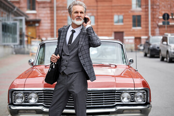 senior businessman left office building to talk on modern mobile phone in the street. handsome od gray haired man 60 years old hearing important information via speed mobile connectivity