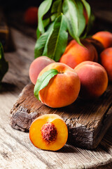 Naklejka na ściany i meble Peaches with leaves on dark wooden board with peach in halves with peach seed stone. Composition with ripe juicy peaches Harvest for food. Fresh organic fruit